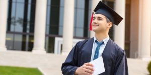 Young graduate in cap and gown holding diploma, looking forward.